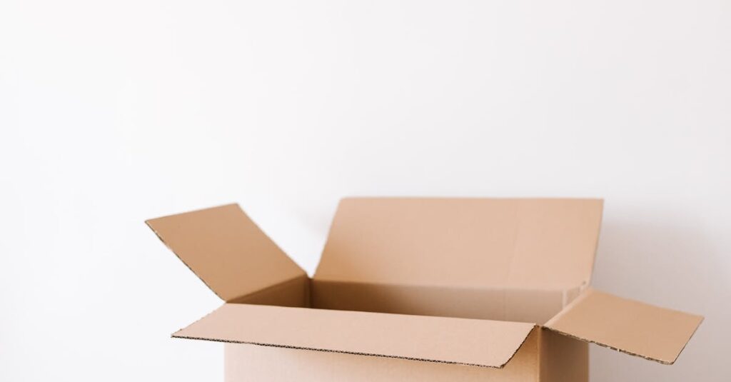 An open cardboard box on a weathered wooden table with tape and scissors beside it, ready for packing.